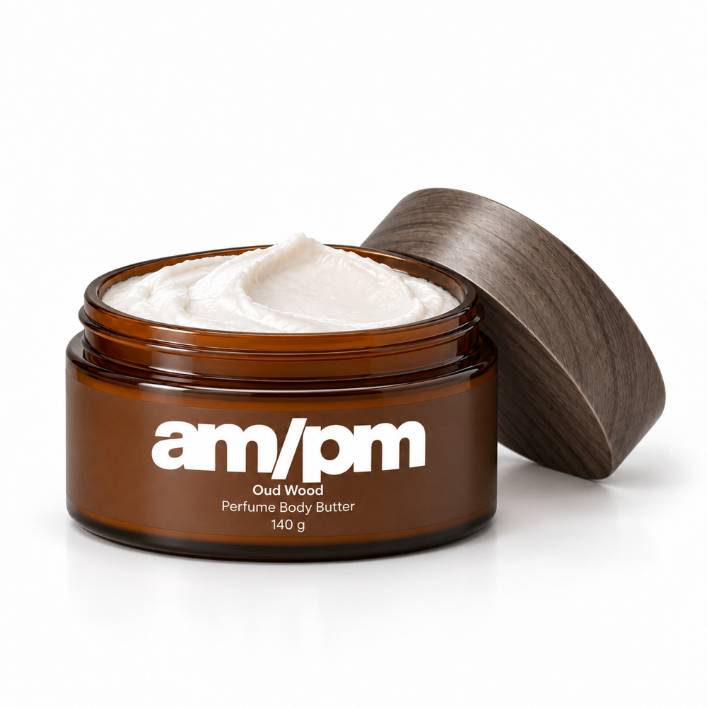 Open AM/PM Oud Wood body butter with thick white cream and its grey-brown woodprint lid resting beside the jar.